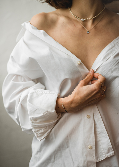 Person wearing necklaces and unbuttoned white shirt.