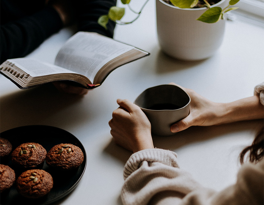 People seated at table reading book and drinking coffee.